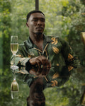 Man sitting at a table with a glass of champagne, surrounded by greenery